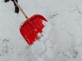 A red shovel being used to shovel snow.