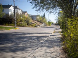A street and sidewalk in Flin Flon leading to houses on the left.
